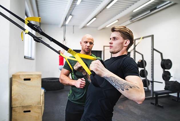 NPE, athlete with a personal trainer in gym doing exercise with TRX