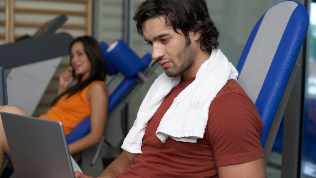 A gym owner building his online fitness store on his laptop with the help of WellnessLiving.