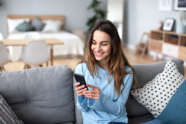 work-life balance, cheerful young woman using mobile phone while sitting on a couch