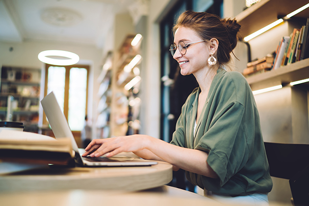 Pilates studio, cheerful young freelance woman typing on laptop in library