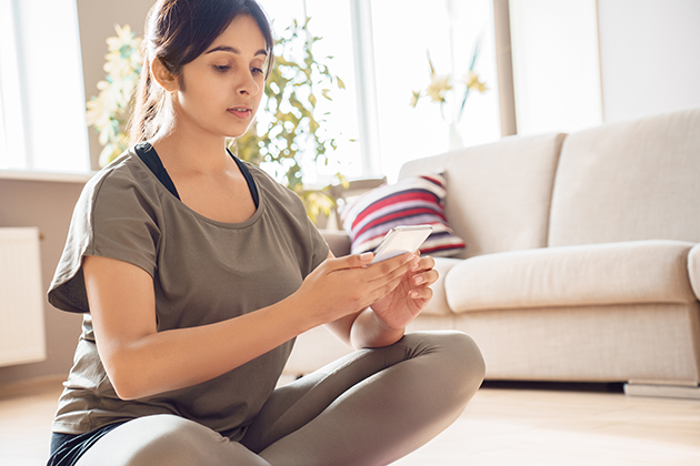 yoga workshops, Indian woman holding smart phone using fitness application at home