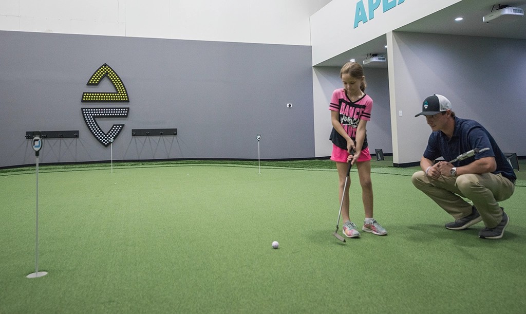 Coach helps little girl golf indoors