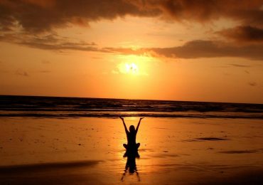 Someone practicing a mindful yoga routine on the beach at sunset.