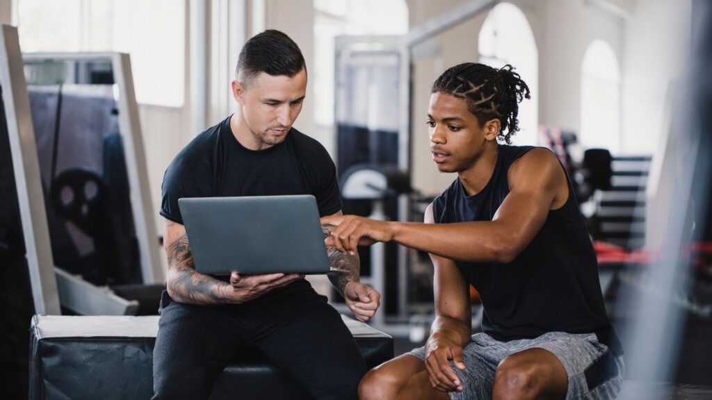 A personal trainer helps his client set up a profile on their new software system.