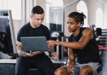 A personal trainer helps his client set up a profile on their new software system.