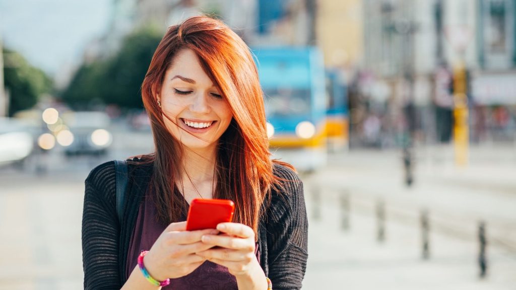 A young person ion a busy city sidewalk receives a text reminder about their upcoming class.