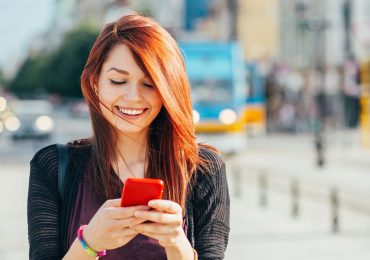 A young person ion a busy city sidewalk receives a text reminder about their upcoming class.