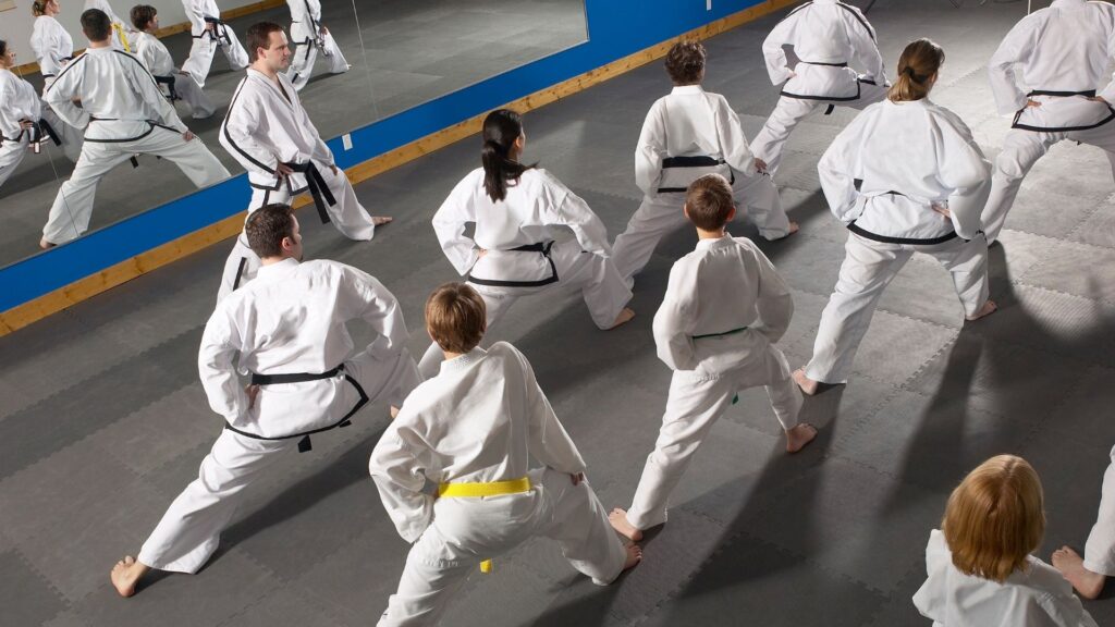 A busy martial arts school begins their class with stretching routines.