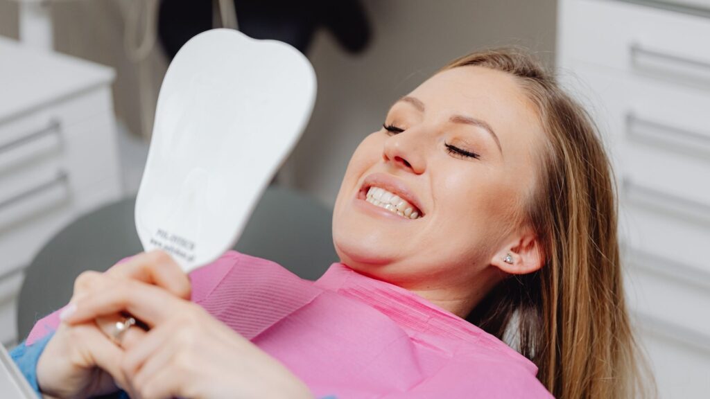A happy client looks at her smile in a mirror after a checkup with her new favorite dental office.