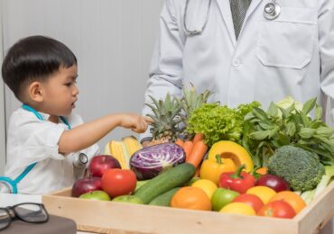 A nutritionist showing a child a variety of colorful fruits and vegetables.