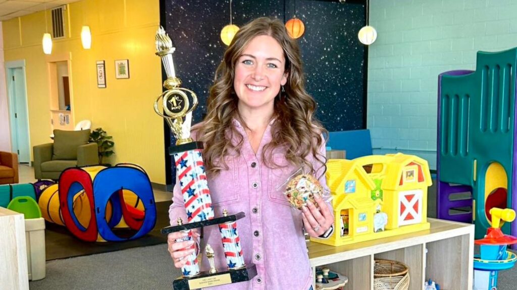 The owner of Nani's Playroom, holding a trophy for their award-winning cookies.