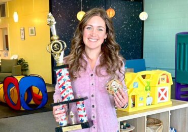 The owner of Nani's Playroom, holding a trophy for their award-winning cookies.