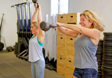 Two women using kettle bells in their women's-only gym, powered by WellnessLiving.