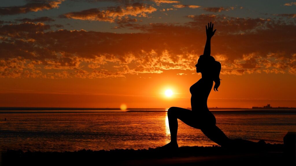 The silhouette of someone from Bikram Yoga Bella Vista doing yoga on a beach.
