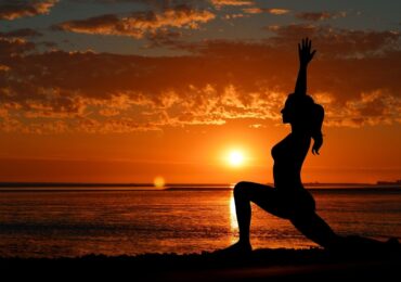 The silhouette of someone from Bikram Yoga Bella Vista doing yoga on a beach.