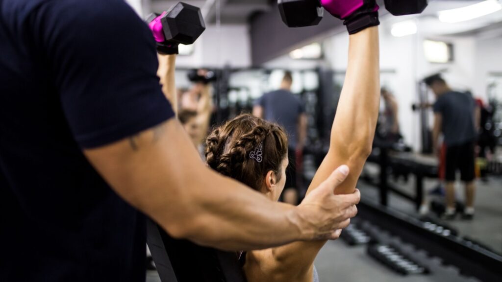 A personal trainer at Fitness and More helps a client through their weight-lifting reps.