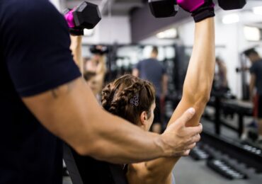 A personal trainer at Fitness and More helps a client through their weight-lifting reps.