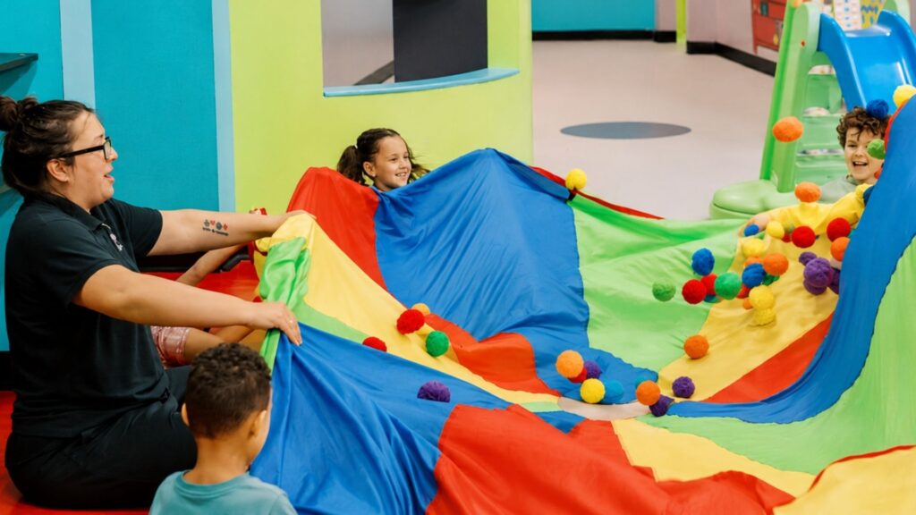 A mother playing with her kids and a colorful parachute at Romp n' Roll.