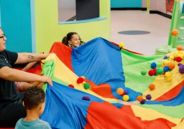 A mother playing with her kids and a colorful parachute at Romp n' Roll.
