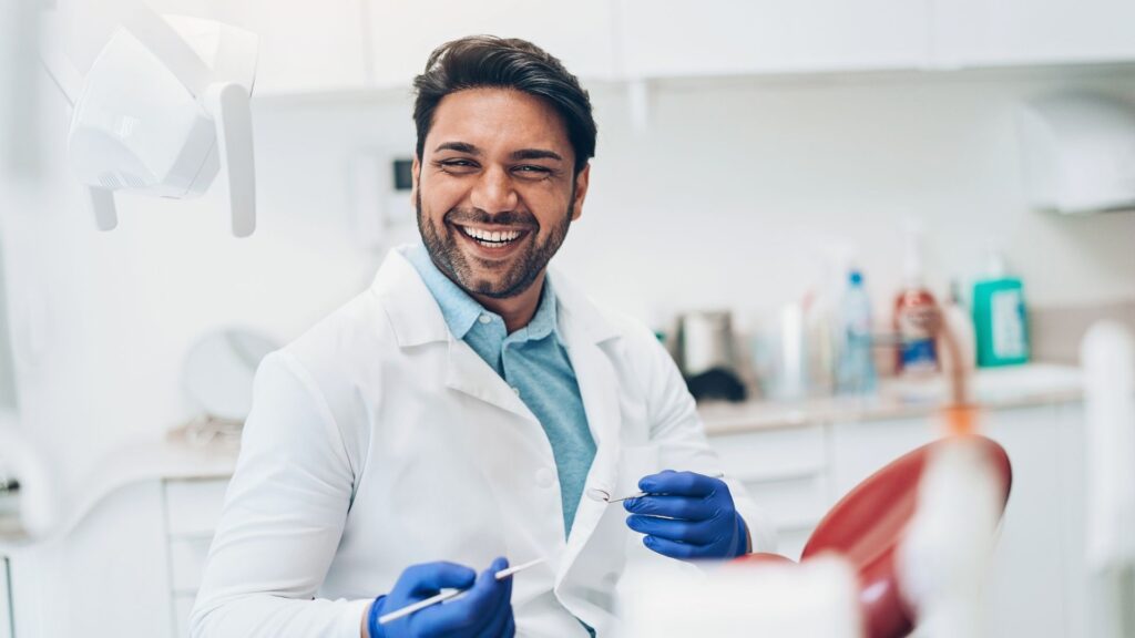 A smiling dentist, welcoming a patient into the dental chair.
