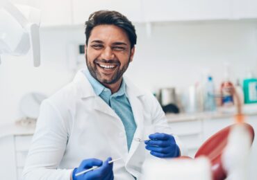 A smiling dentist, welcoming a patient into the dental chair.