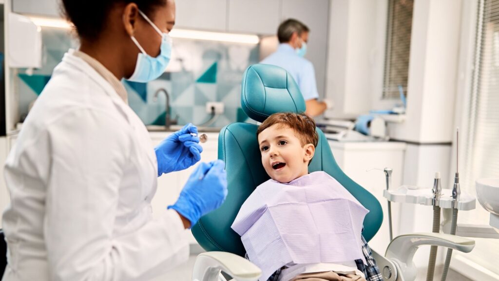 A dentist holding tools while a young patient shows their smile.