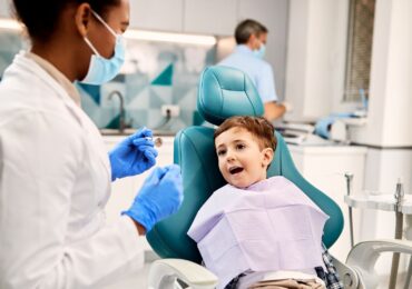 A dentist holding tools while a young patient shows their smile.
