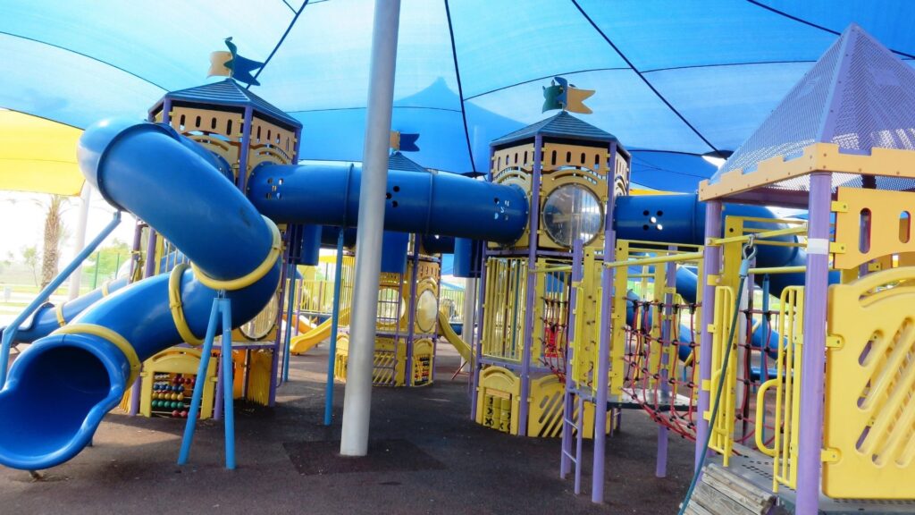 A colorful outdoor, commercial playground covered by a blue tent canopy.
