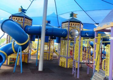 A colorful outdoor, commercial playground covered by a blue tent canopy.