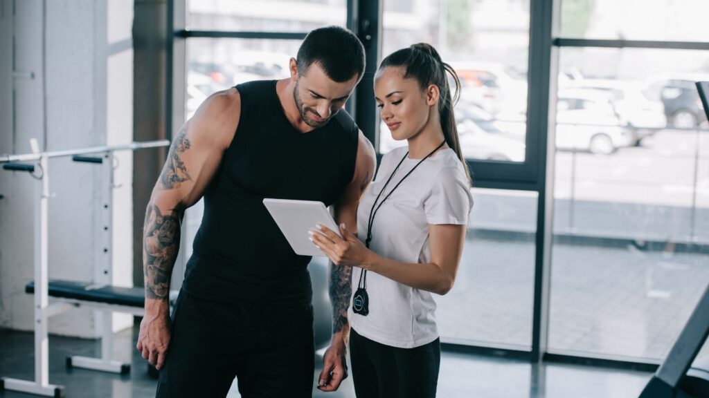 A gym owner helps a client check in on their tablet, with WellnessLiving's gym CRM software.