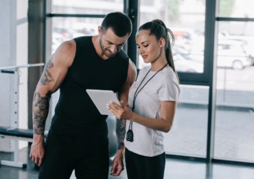 A gym owner helps a client check in on their tablet, with WellnessLiving's gym CRM software.