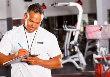 A gym owner taking down manual notes on class attendance because he doesn't have a gym analytics software system.